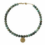 Collier en jaspe turquoise africain avec médaille œil dorée porté sur fond blanc