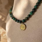 Collier en jaspe turquoise africain avec médaille œil dorée porté sur buste