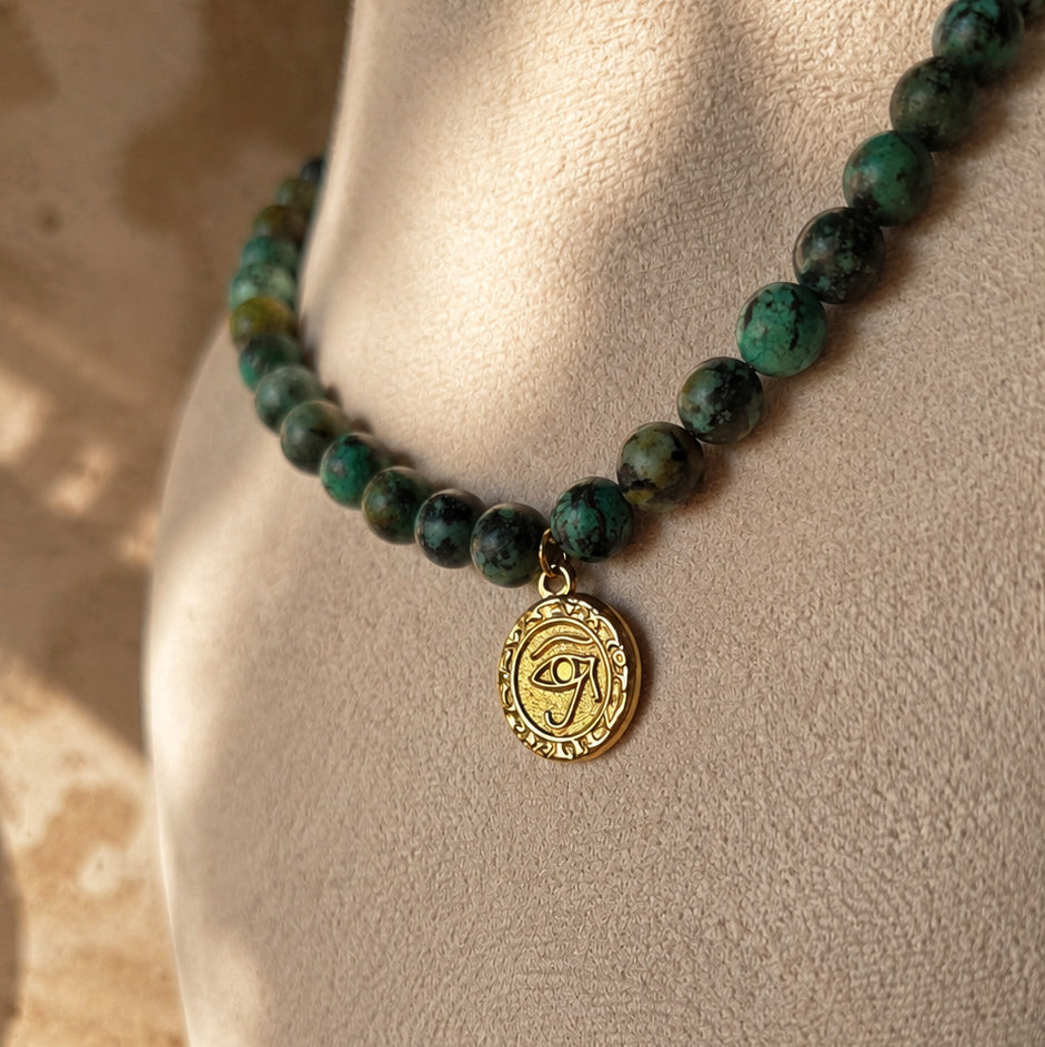 Collier en jaspe turquoise africain avec médaille œil dorée porté sur buste