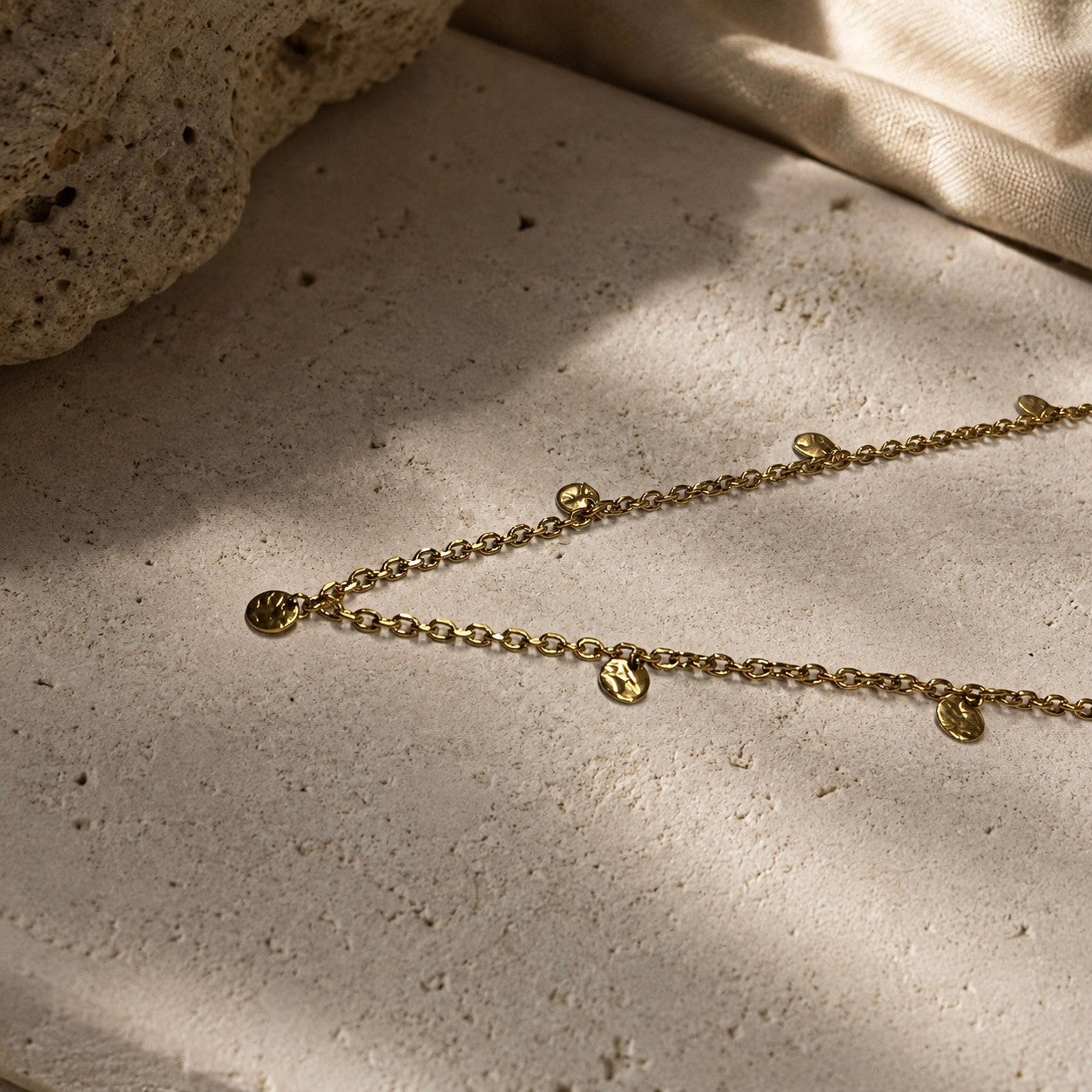 Collier long doré à pampilles rondes dans un décor minéral