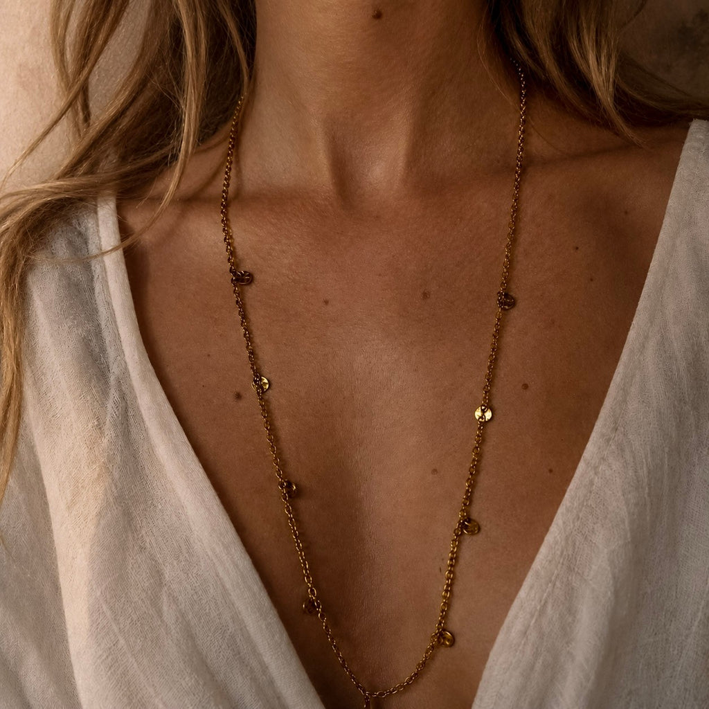 Collier long doré à pampilles martelées porté sur un décolleté