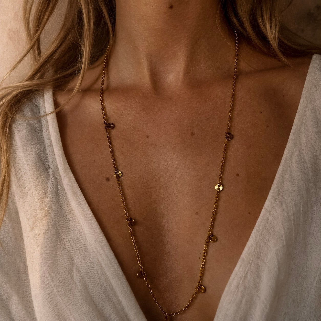 Collier long doré à pampilles martelées porté sur un décolleté