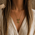 Collier doré en acier inoxydable avec pierres de malachite et pendentif médaillon, porté avec une blouse blanche dans un style bohème chic.