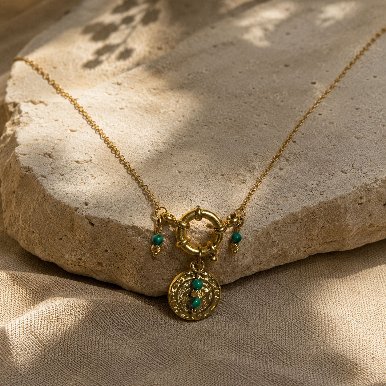 Détail d’un collier doré avec fermoir rond, médaille oeil et perles de malachite