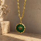 Collier doré avec pendentif abeille vert présenté dans un décor naturel