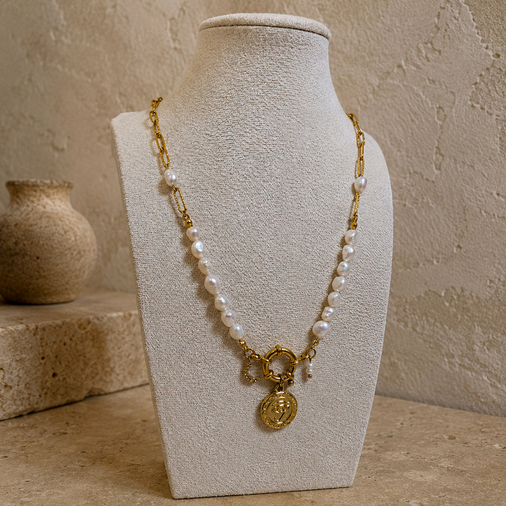 Détail d’un collier en perles d’eau douce avec fermoir doré, pendentif oeil et breloque lune
