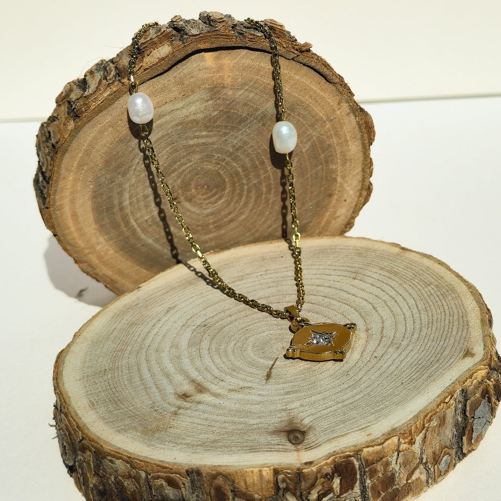 Collier en acier inoxydable doré avec perles d’eau douce et pendentif étoilé présenté sur un support en bois