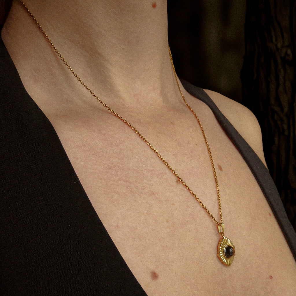 Collier doré pour femme en acier inoxydable avec pendentif soleil et pierre œil de tigre naturelle, porté sur peau nue — bijou protecteur et lumineux signé Clyvia Bijoux.