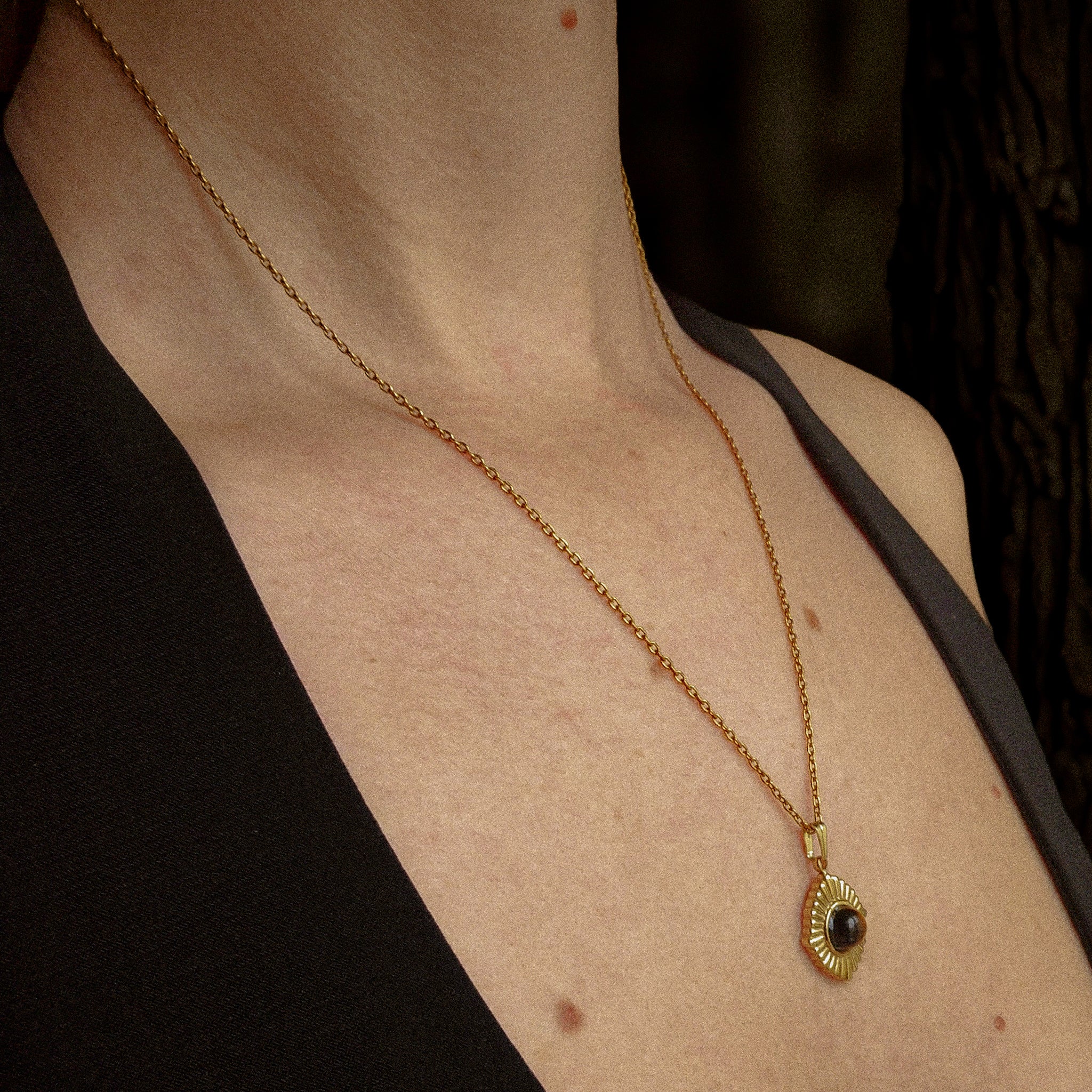 Collier doré pour femme en acier inoxydable avec pendentif soleil et pierre œil de tigre naturelle, porté sur peau nue — bijou protecteur et lumineux signé Clyvia Bijoux.