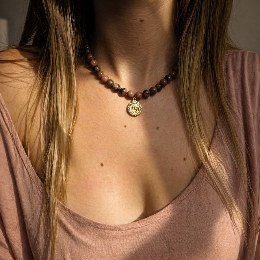 Collier en rhodonite naturelle porté au cou avec médaille dorée