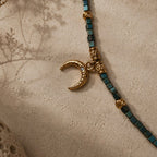 Détail du pendentif lune doré avec perles en verre aux reflets bleu-vert