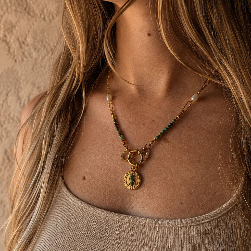 Collier porté en turquoise africaine avec chaîne dorée, perles blanches, pendentif oeil et breloque lune
