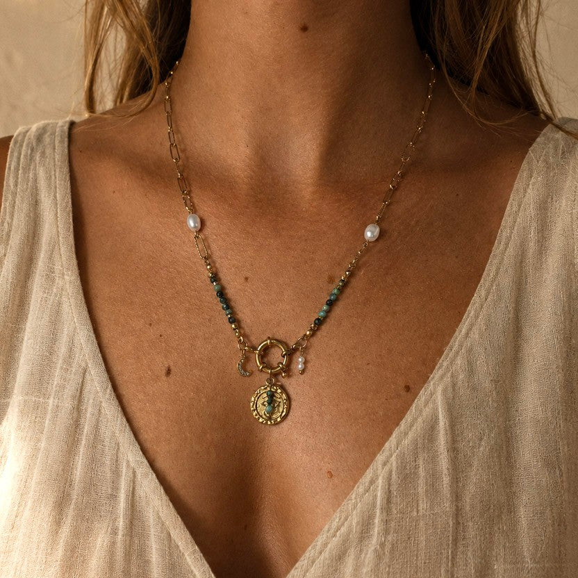 Collier porté en turquoise africaine avec chaîne dorée, perles blanches, pendentif oeil et breloque lune