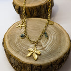 Collier doré en acier inoxydable décoré d’une fleur et d’une étoile de mer, avec perles naturelles en jaspe africaine, présenté sur support bois – création Clyvia Bijoux.