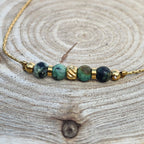 Détail d’un bracelet fin avec pierres de jaspe bleu-vert et finitions dorées en acier inoxydable