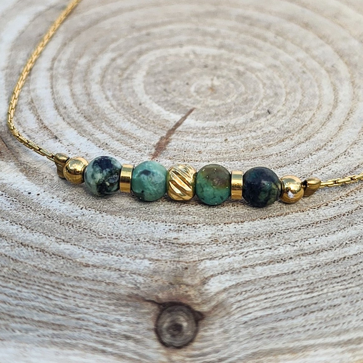 Détail d’un bracelet fin avec pierres de jaspe bleu-vert et finitions dorées en acier inoxydable